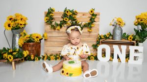 Sunflower themed first birthday photo setup with wooden backdrop and rustic decorations.
