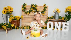 Sunflower themed first birthday photo setup with wooden backdrop and rustic decorations.