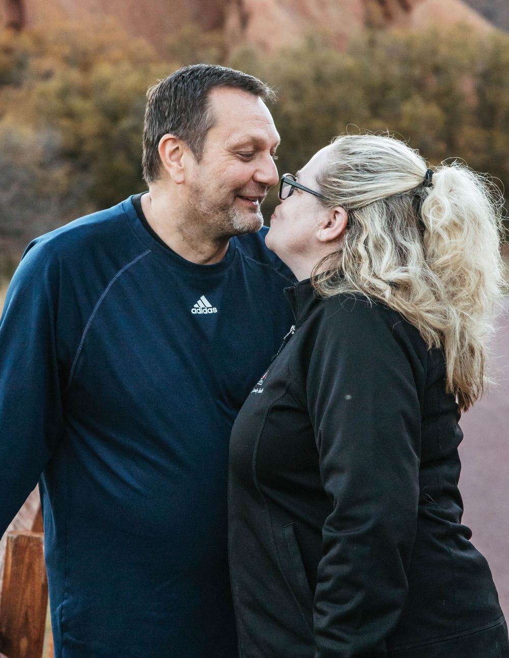 A loving couple shares an intimate moment outdoors with mountains and fall foliage in the background.