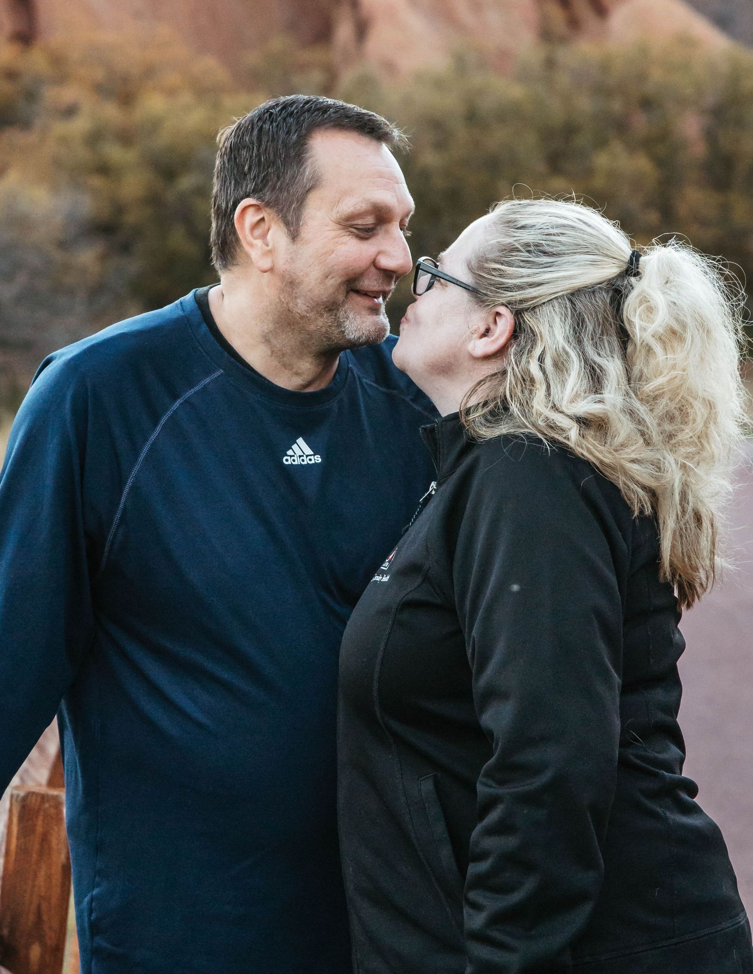 A loving couple shares an intimate moment outdoors with mountains and fall foliage in the background.