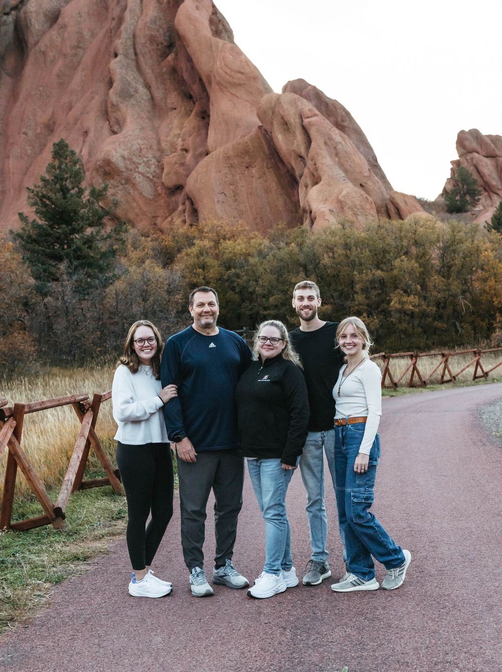 A group poses together on a path at Garden of the Gods park in Colorado with towering red rock formations behind them.