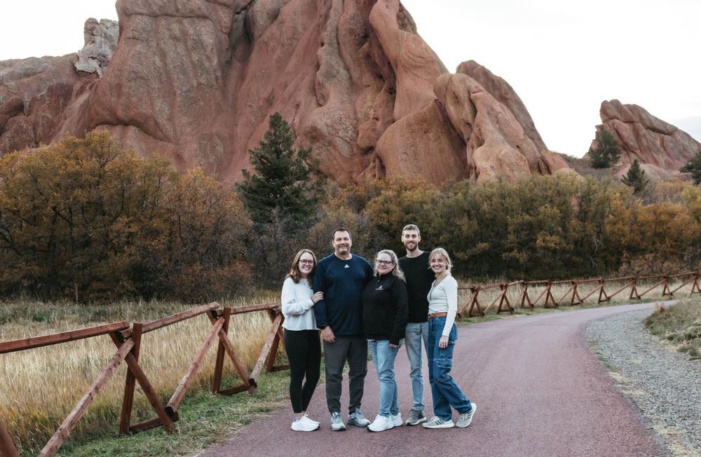 A group of people pose on a paved trail with dramatic red rock formations at Roxborough State Park in Colorado.