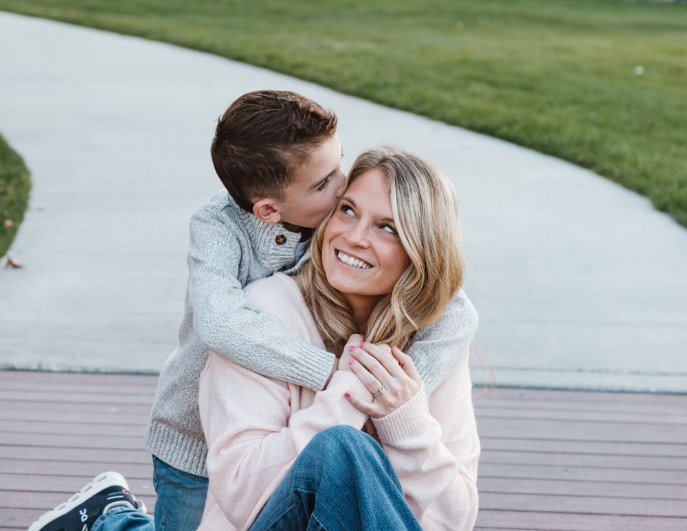 A couple shares an affectionate moment together while sitting outdoors on a pathway surrounded by grass.