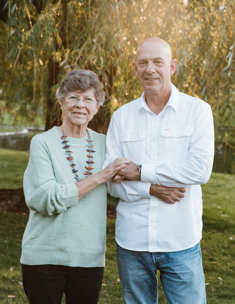 An outdoor portrait of two generations in matching mint and white sweaters standing together in a garden.