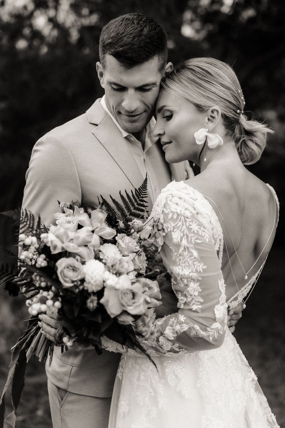 Hochzeitspaar in eleganter Kleidung umarmt sich und hält einen üppigen Blumenstrauß in den Händen.