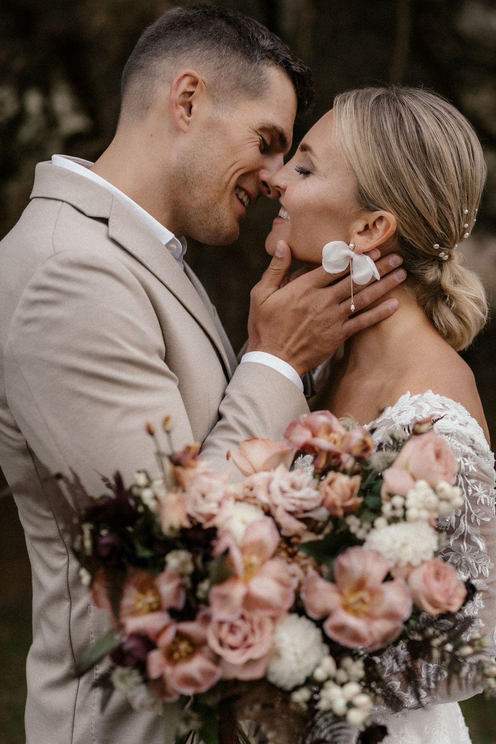 Intimes Hochzeitsporträt, das einen zärtlichen Moment zwischen dem Paar mit einem zartrosa Rosenstrauß zeigt.