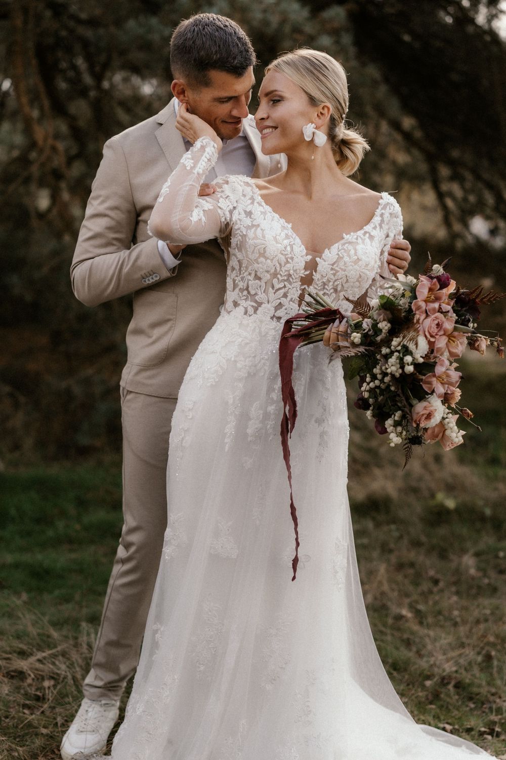 Intimer Hochzeitsmoment im Freien mit einem Paar in beige-weißer Kleidung und einem Blumenstrauß.