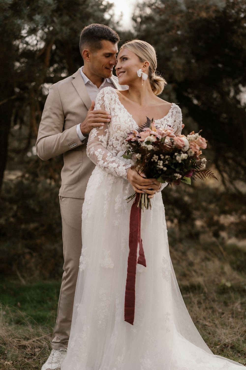 Ungestelltes Hochzeitsporträt im Freien mit dem Paar und einem Blumenarrangement in Rosa und Burgunderrot.