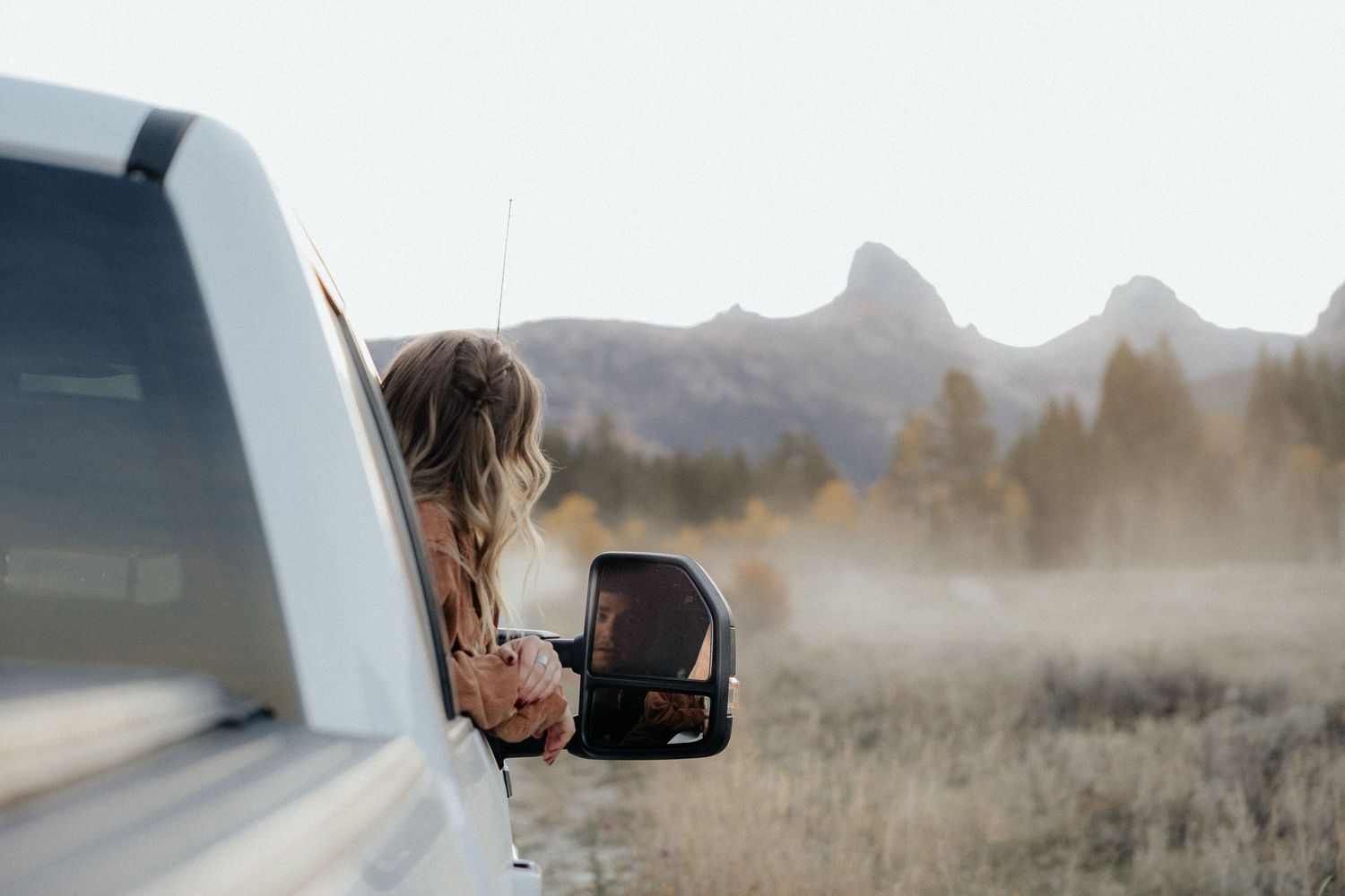 Someone leans out of a truck window against a misty mountain landscape.