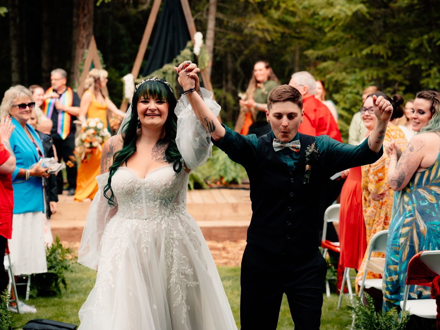 Wedding party laughs and dances together during outdoor reception celebration at garden venue.