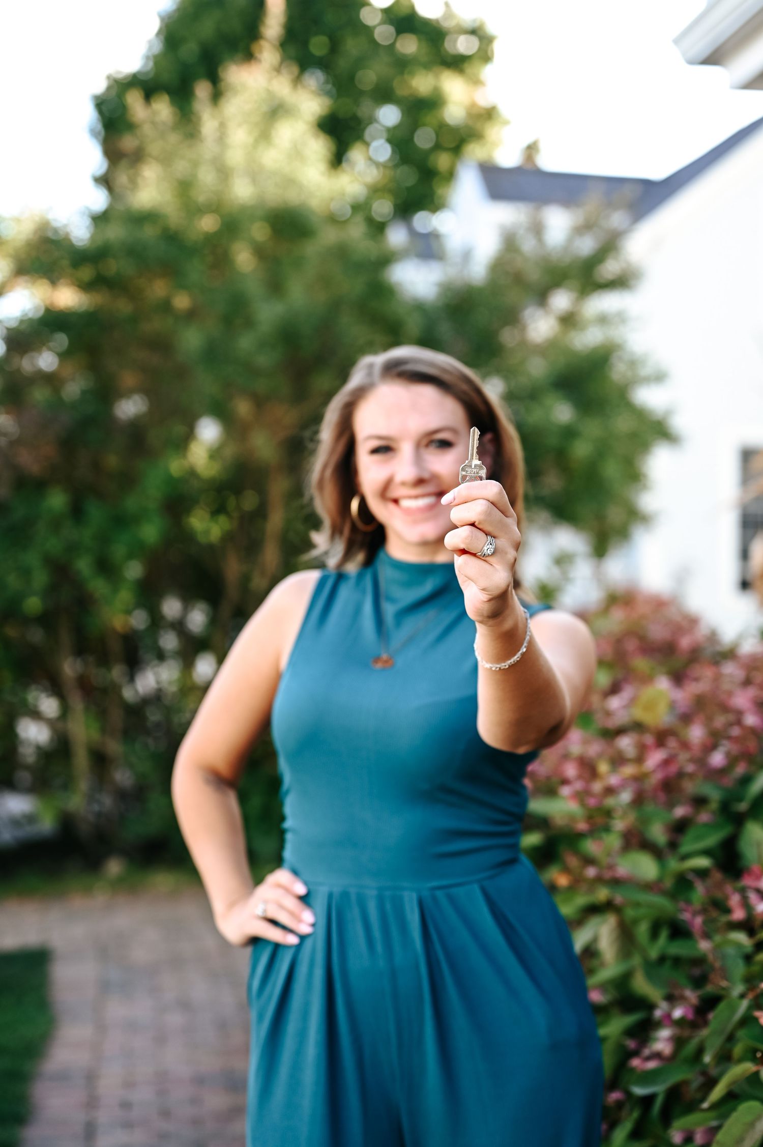 Woman in teal dress posing confidently outdoors with thumbs up gesture.