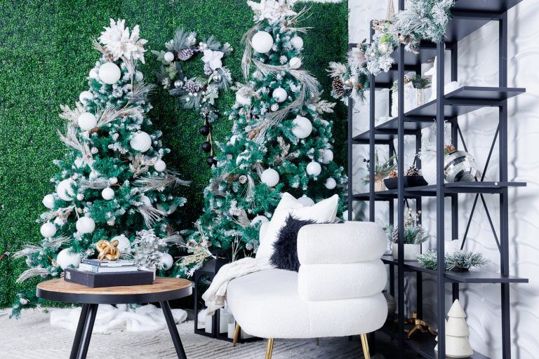 White flocked Christmas trees and modern white chair against a green wall with industrial shelving.