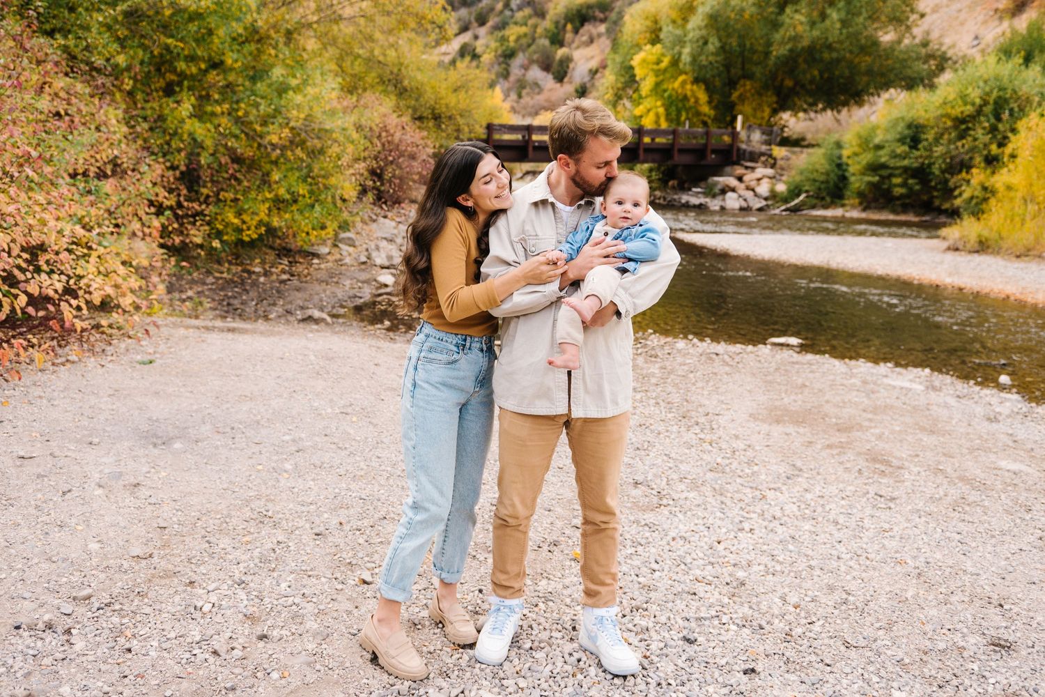 A riverside photo session on a gravel path captures a sweet family moment in casual attire.