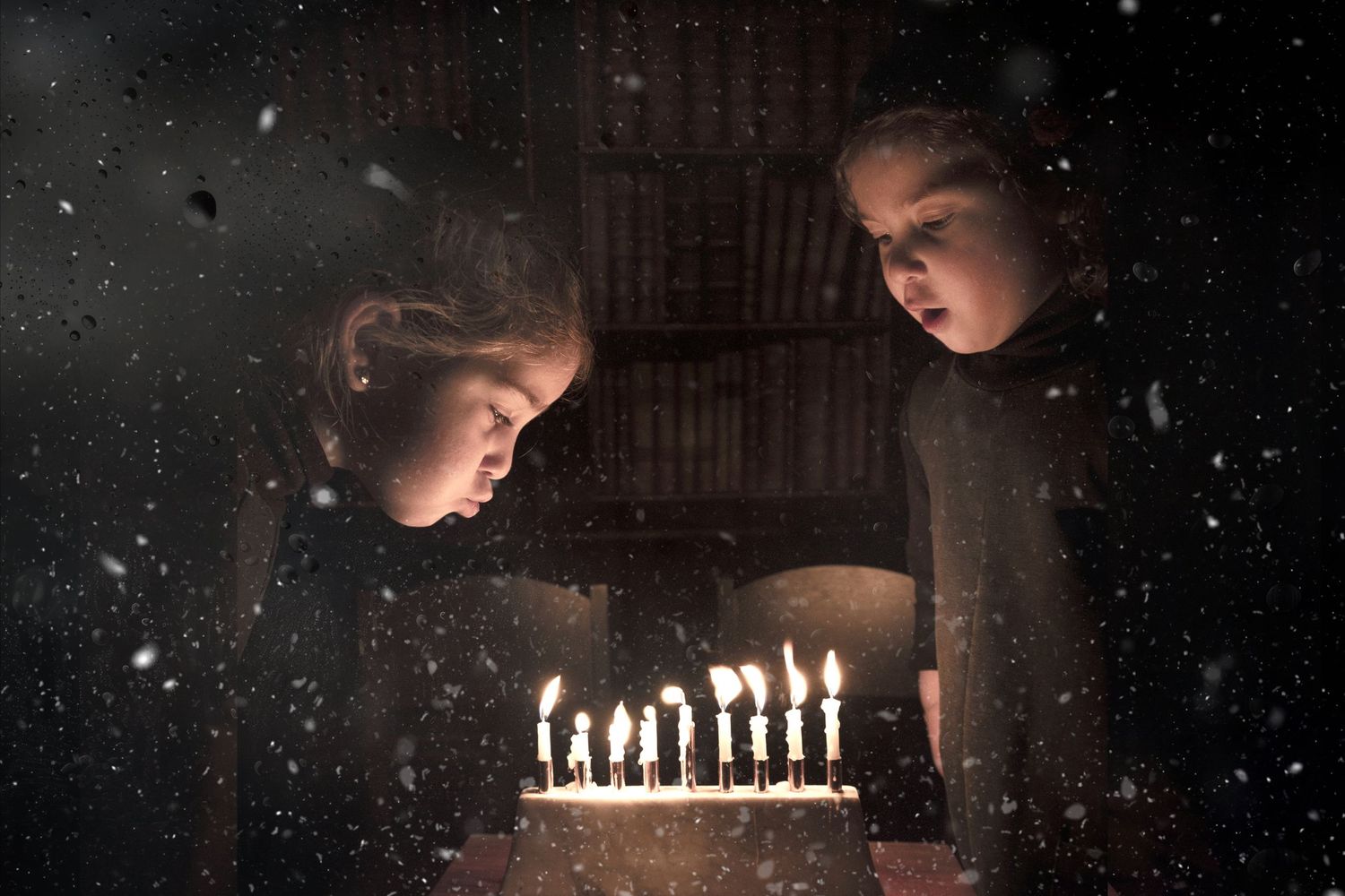 Two figures gaze at glowing candles in a dark room with snow visible through window.
