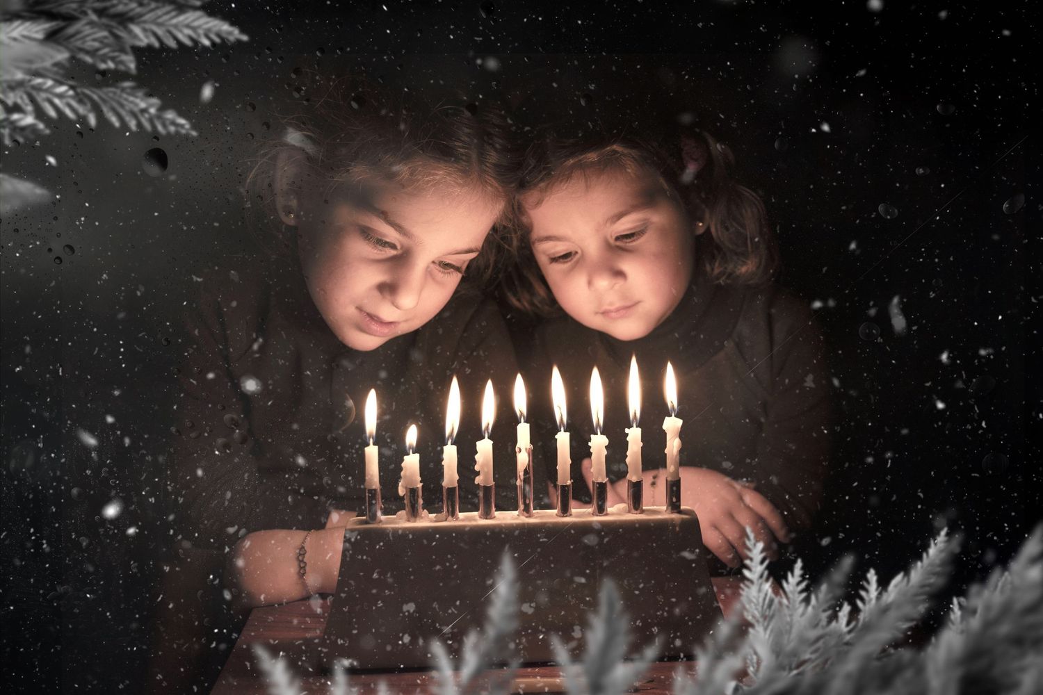 Two figures lean over a cake with lit candles while snow falls outside the window.