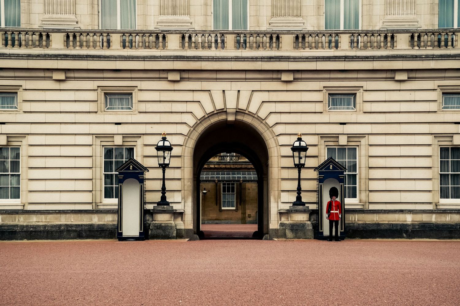 Ornate entrance to Buckingham Palace with guards standing at attention beside traditional lampposts.