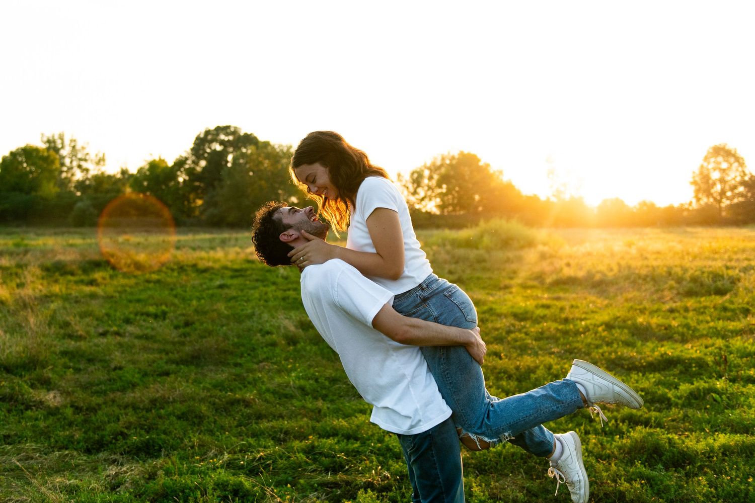 A couple embraces in a golden meadow during sunset as they share a romantic moment in the warm evening light.