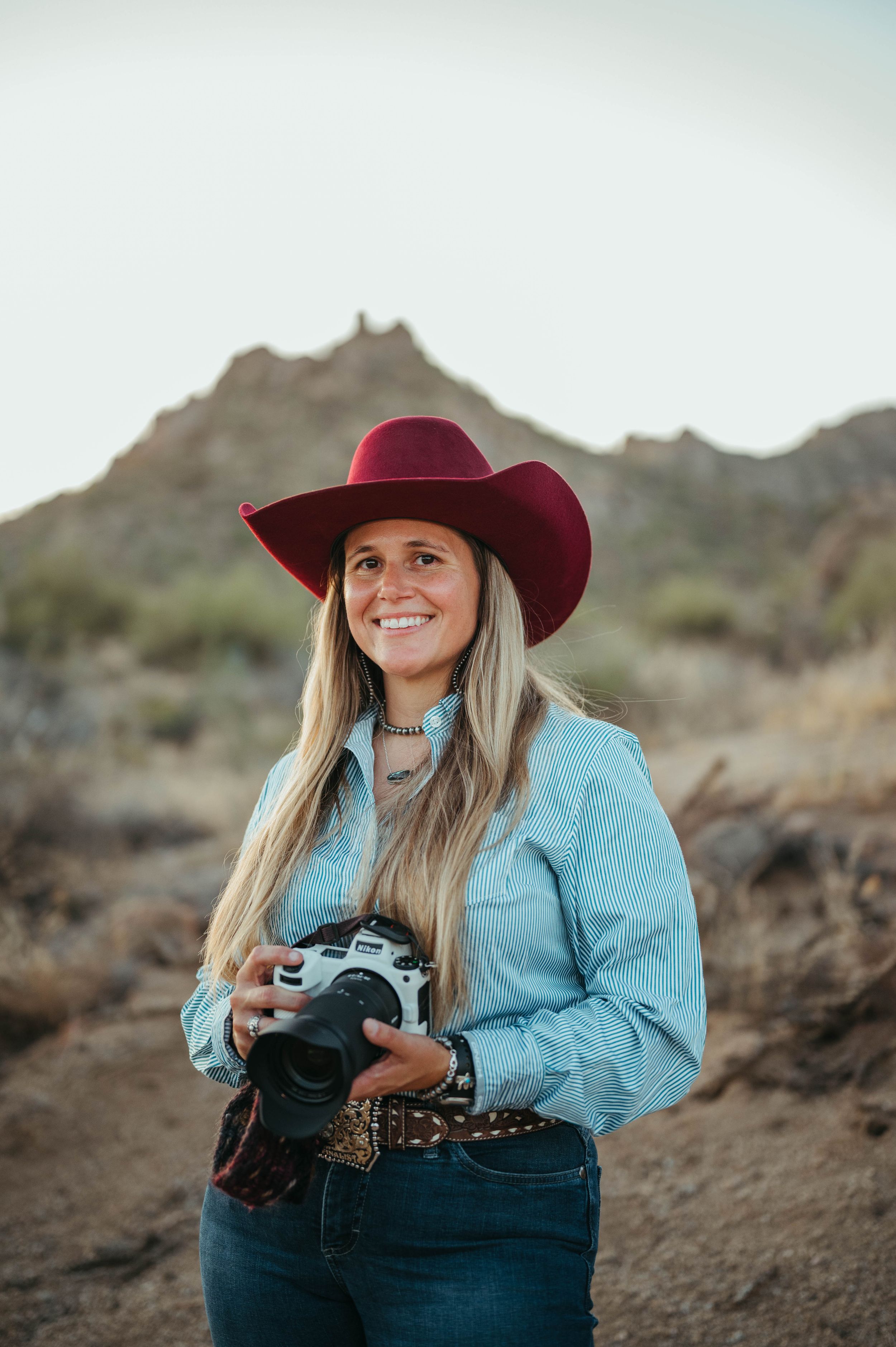 Desert photographer in red cowboy hat and blue shirt holding vintage camera.