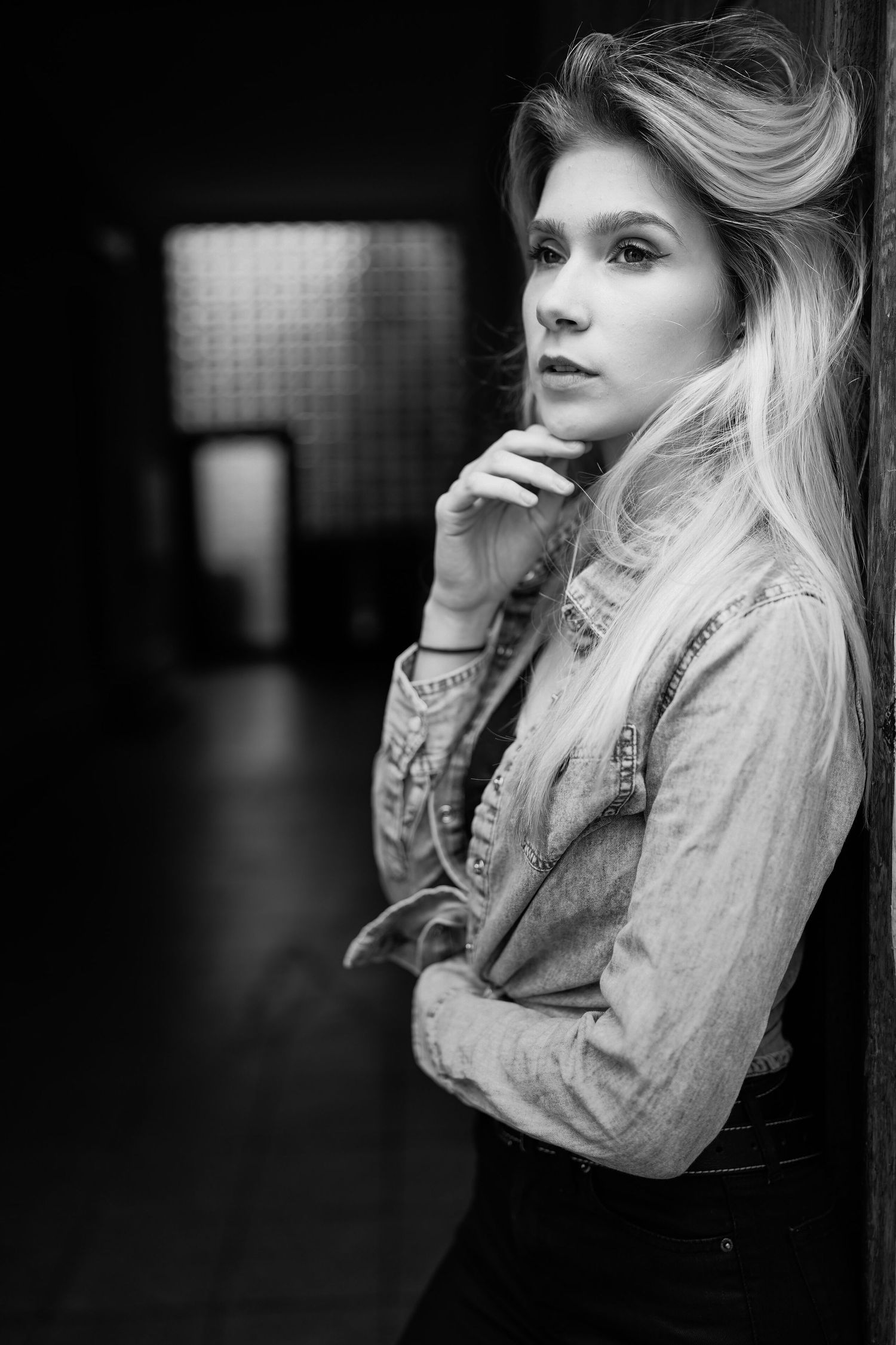 Dramatisches Schwarz-Weiß-Porträt einer Frau in Jeansjacke mit langen blonden Haaren vor dunklem Hintergrund.
