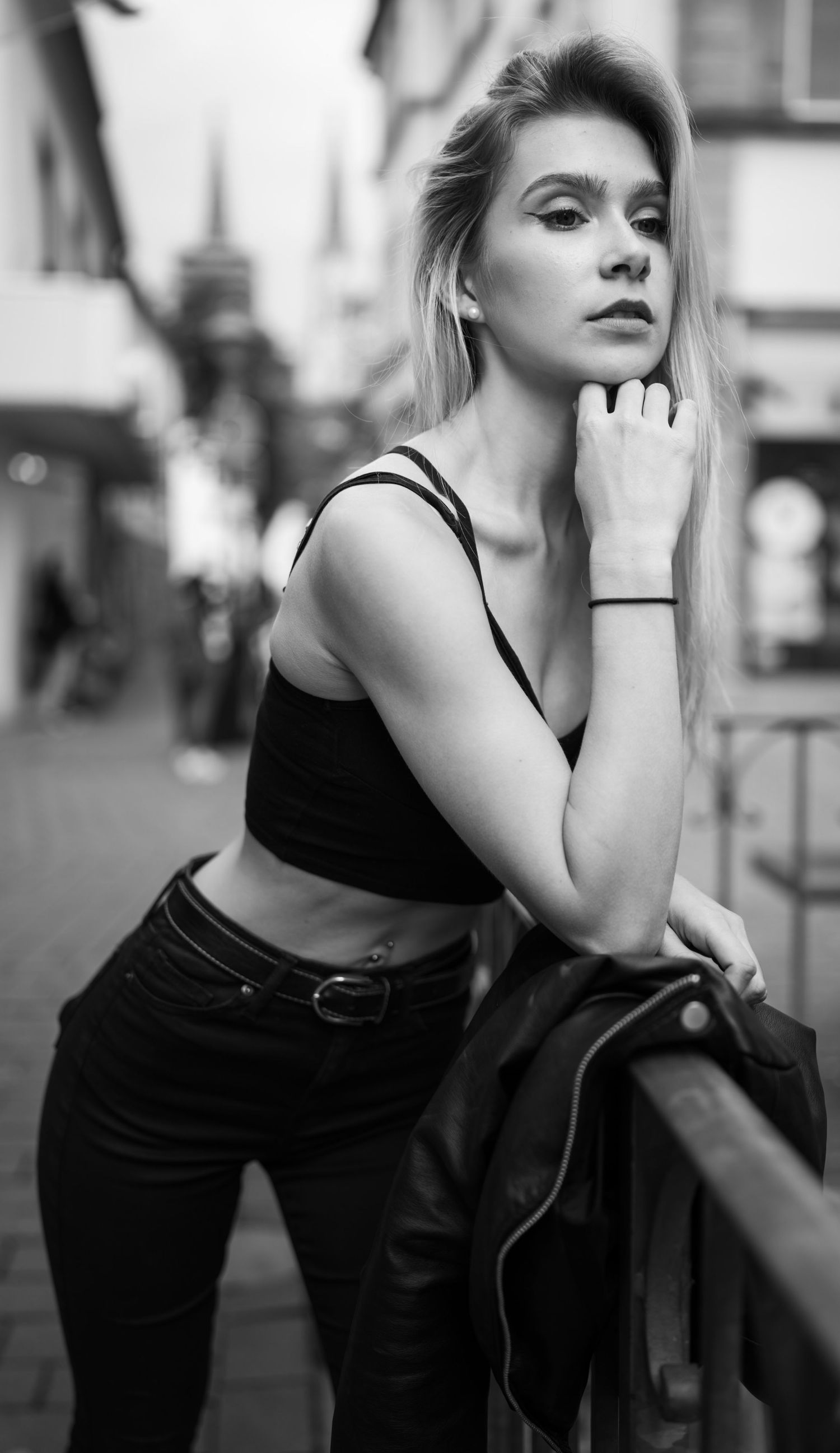 Streetfashion-Porträt einer Frau in schwarzem bauchfreiem Top und Jeans, die an einem Geländer lehnt.