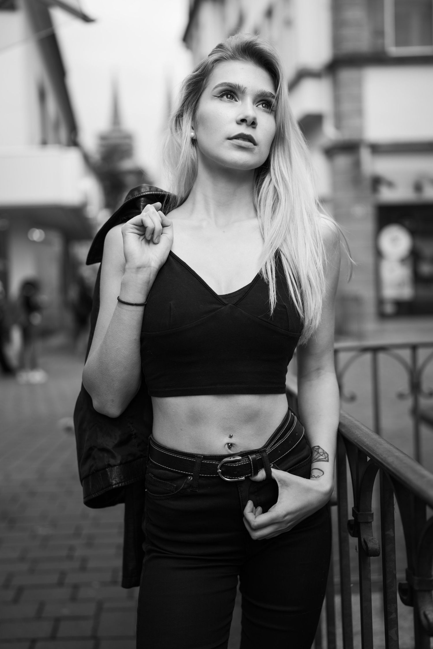 Urbanes Porträt einer Frau in schwarzem bauchfreiem Top und hoch taillierten Jeans auf einer Stadtstraße.
