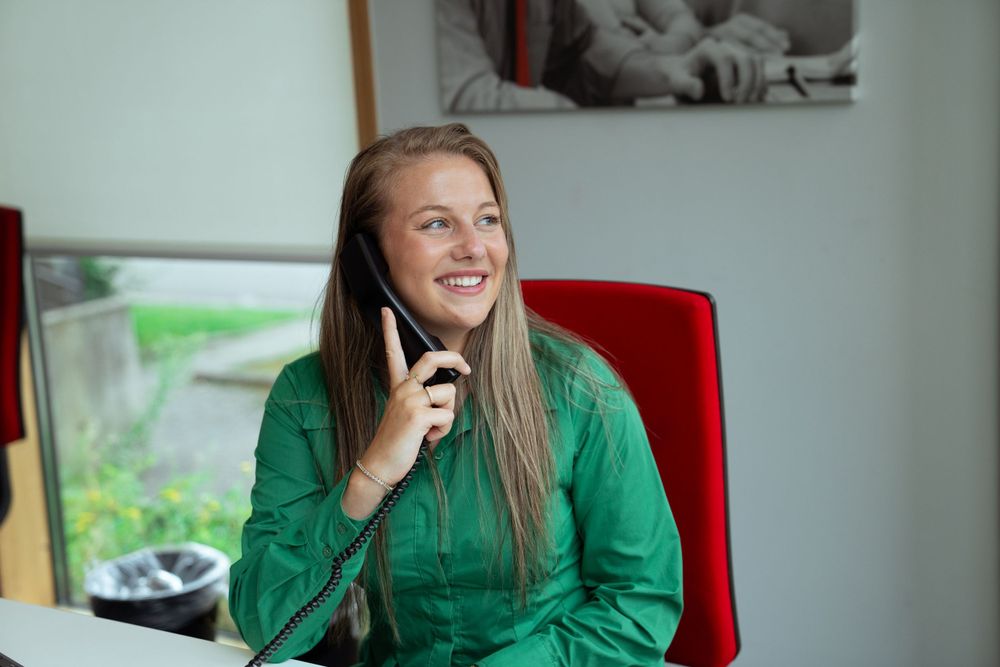 Business portrait of a woman holding a phone at her desk, smiling and looking professional in Hasselt.