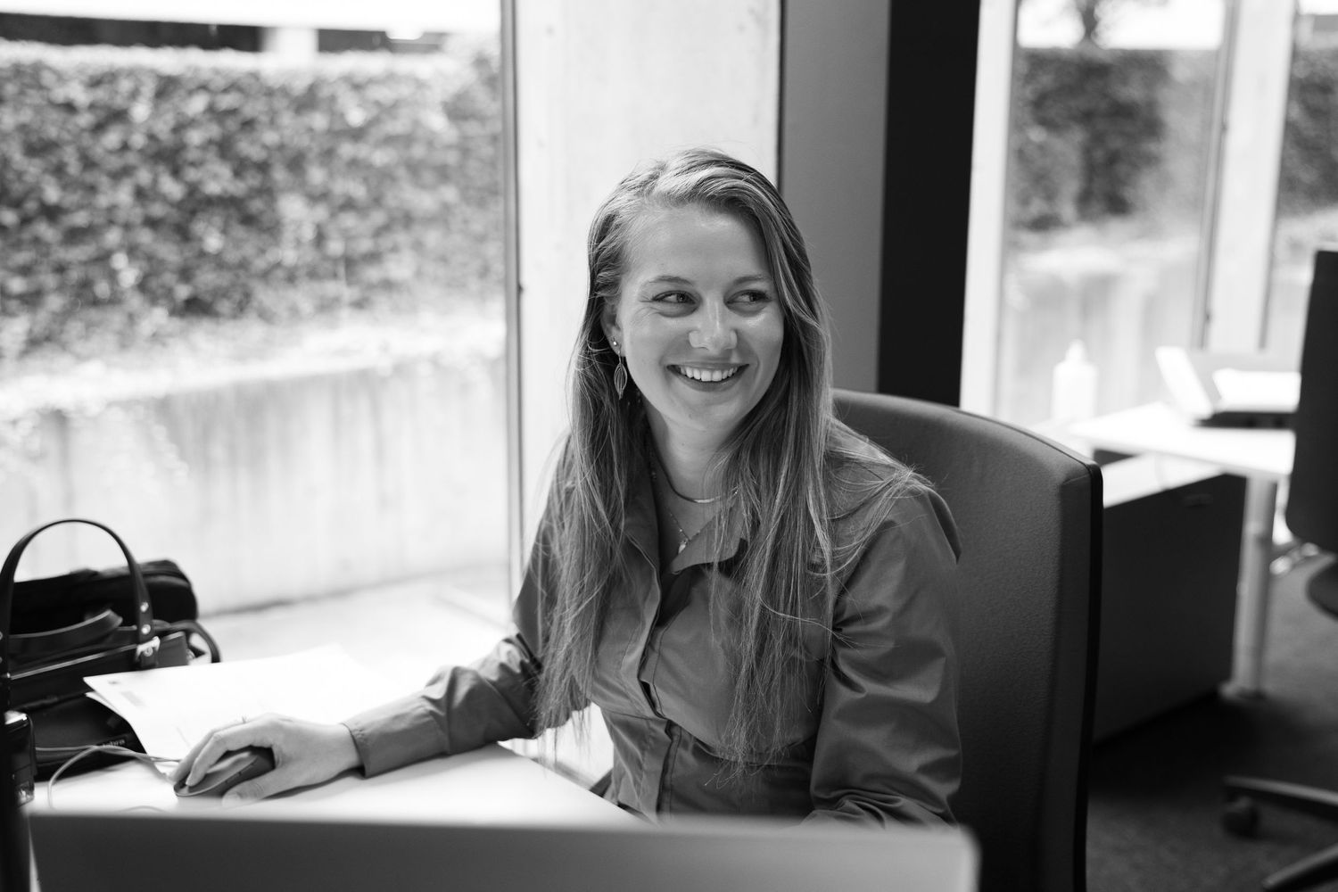 Happy woman sitting at her desk with a computer, smiling and working in a professional setting in Hasselt.