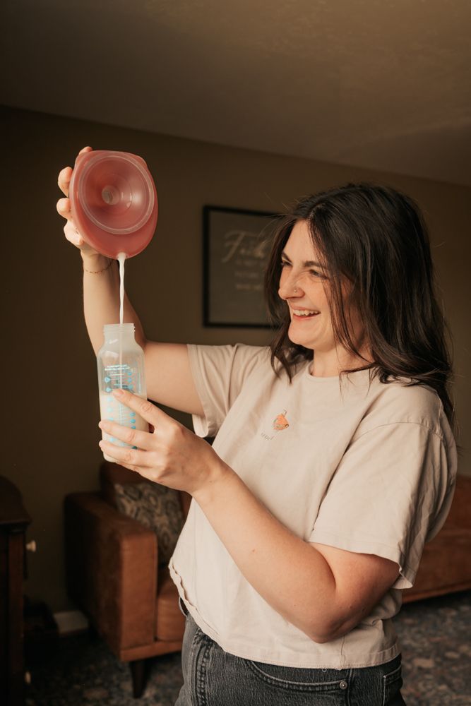 Person in white shirt smiles while holding a glass jar and measuring ingredients in a dimly lit room.
