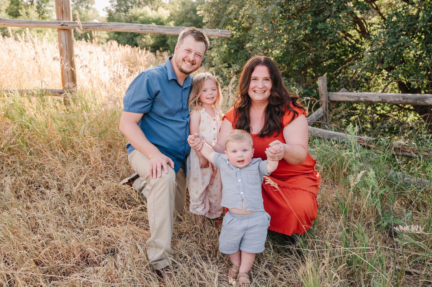 A family in casual attire poses together on a grassy hillside during a sunny outdoor photo session.