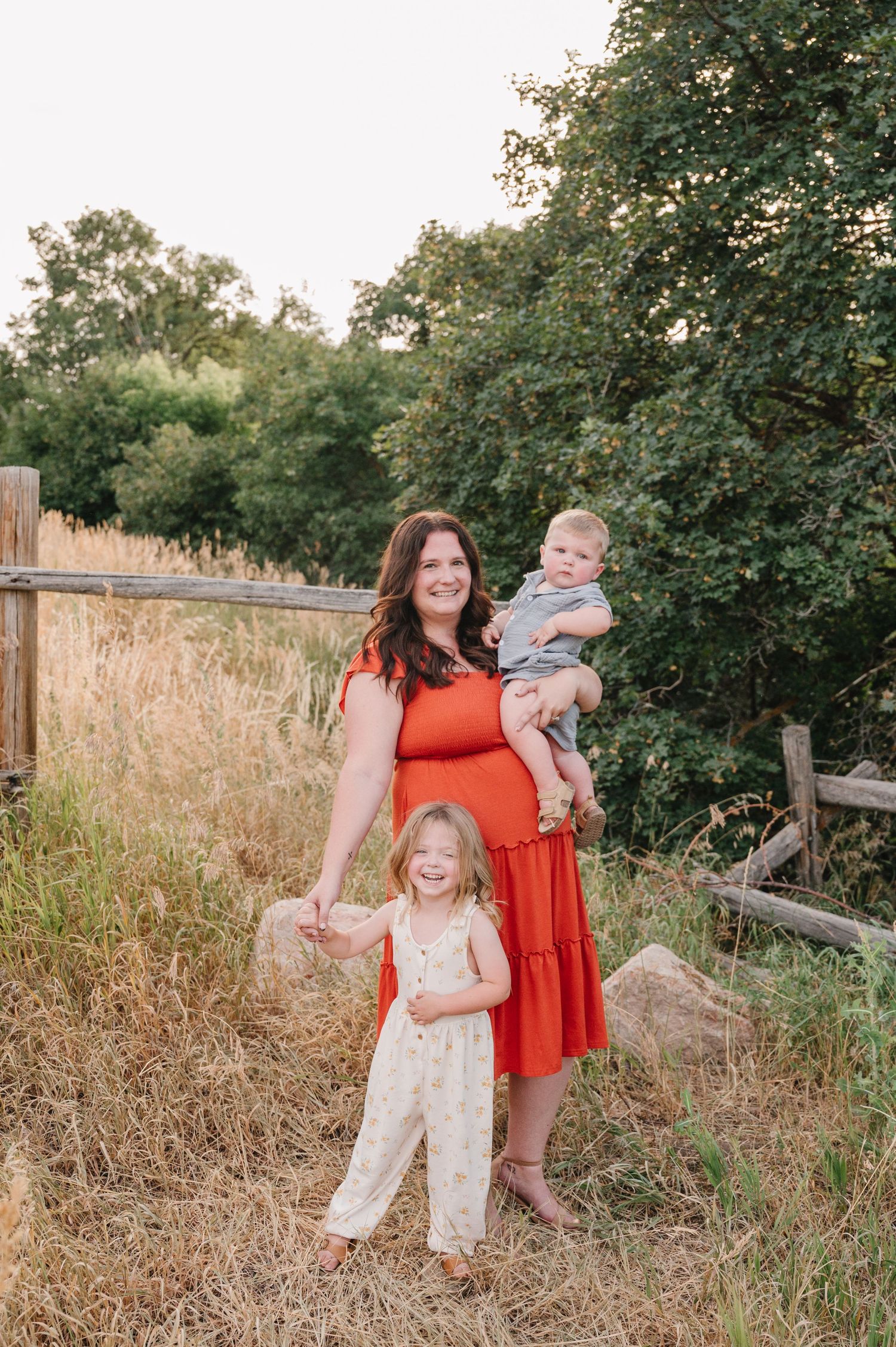 A family portrait in a golden field next to a rustic wooden fence during sunset.