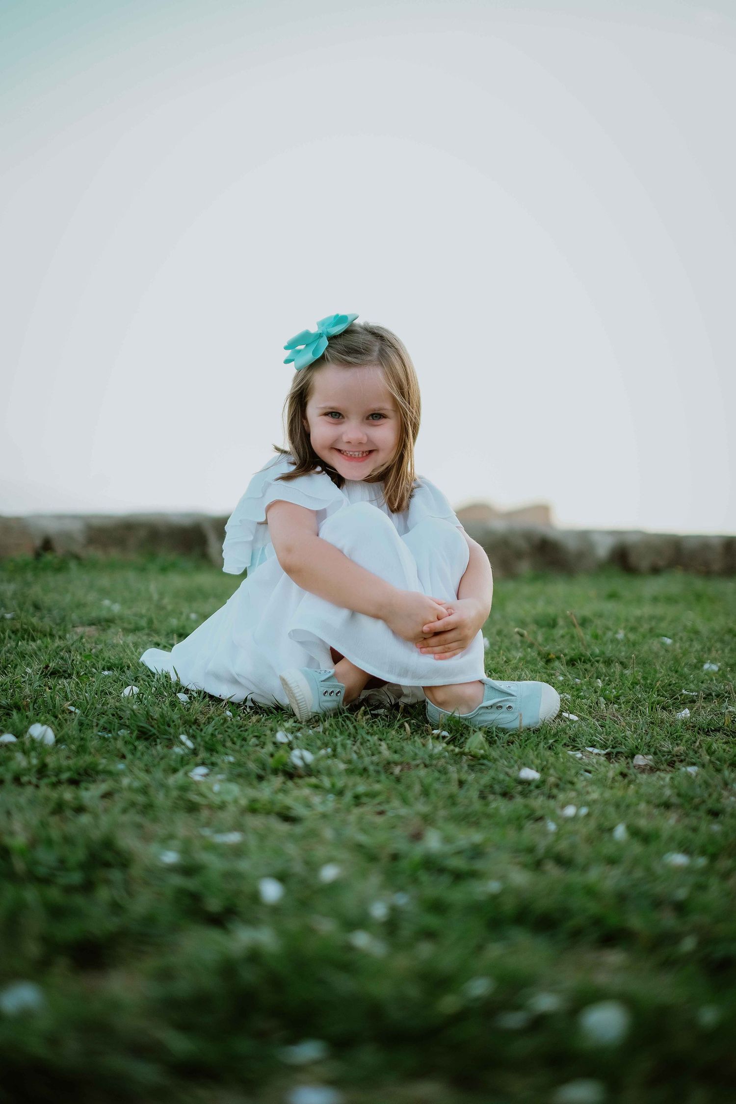 Child in white dress rolling on green grass with playful energy.
