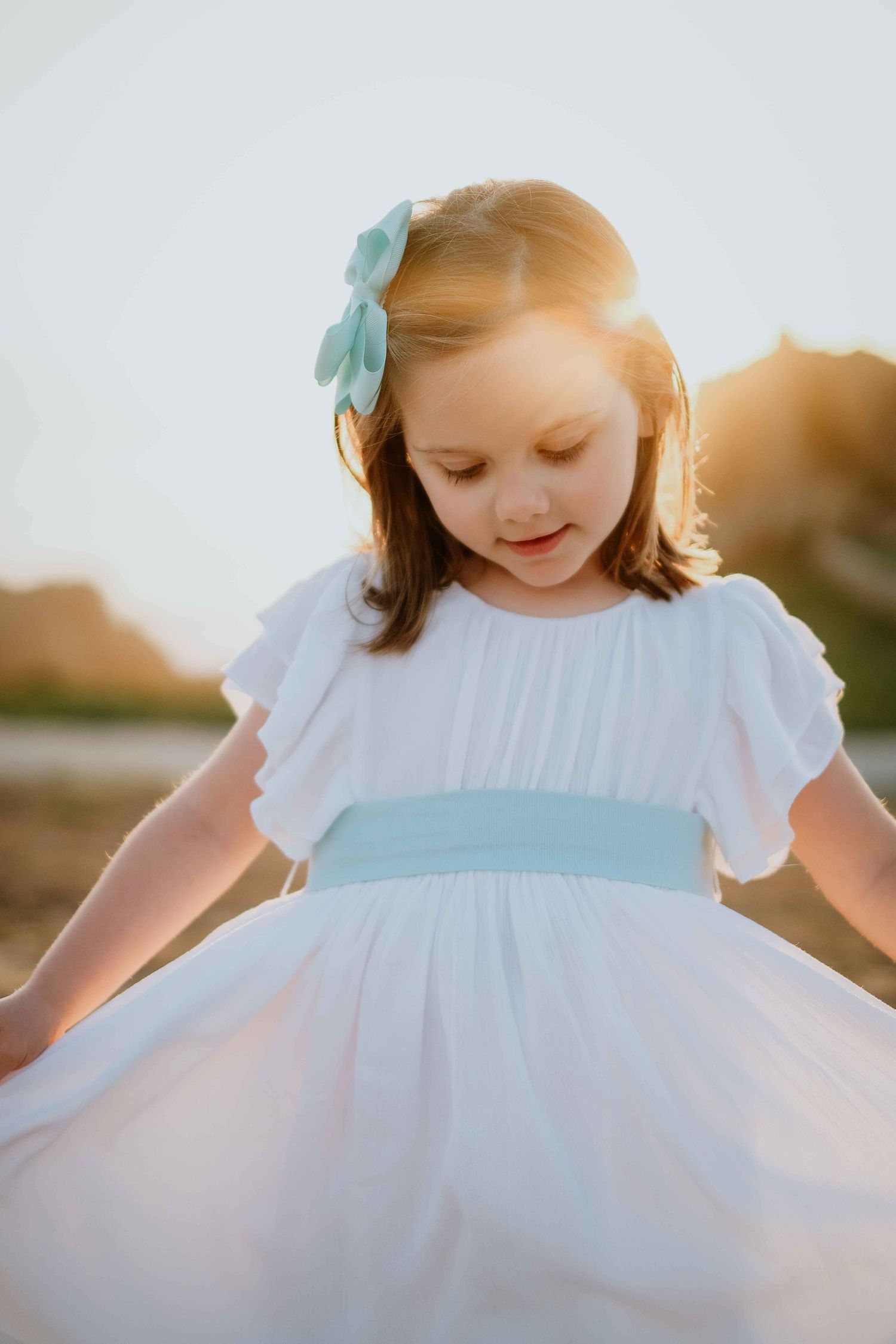 Child in white dress playing in golden sunlight with joyful expression.