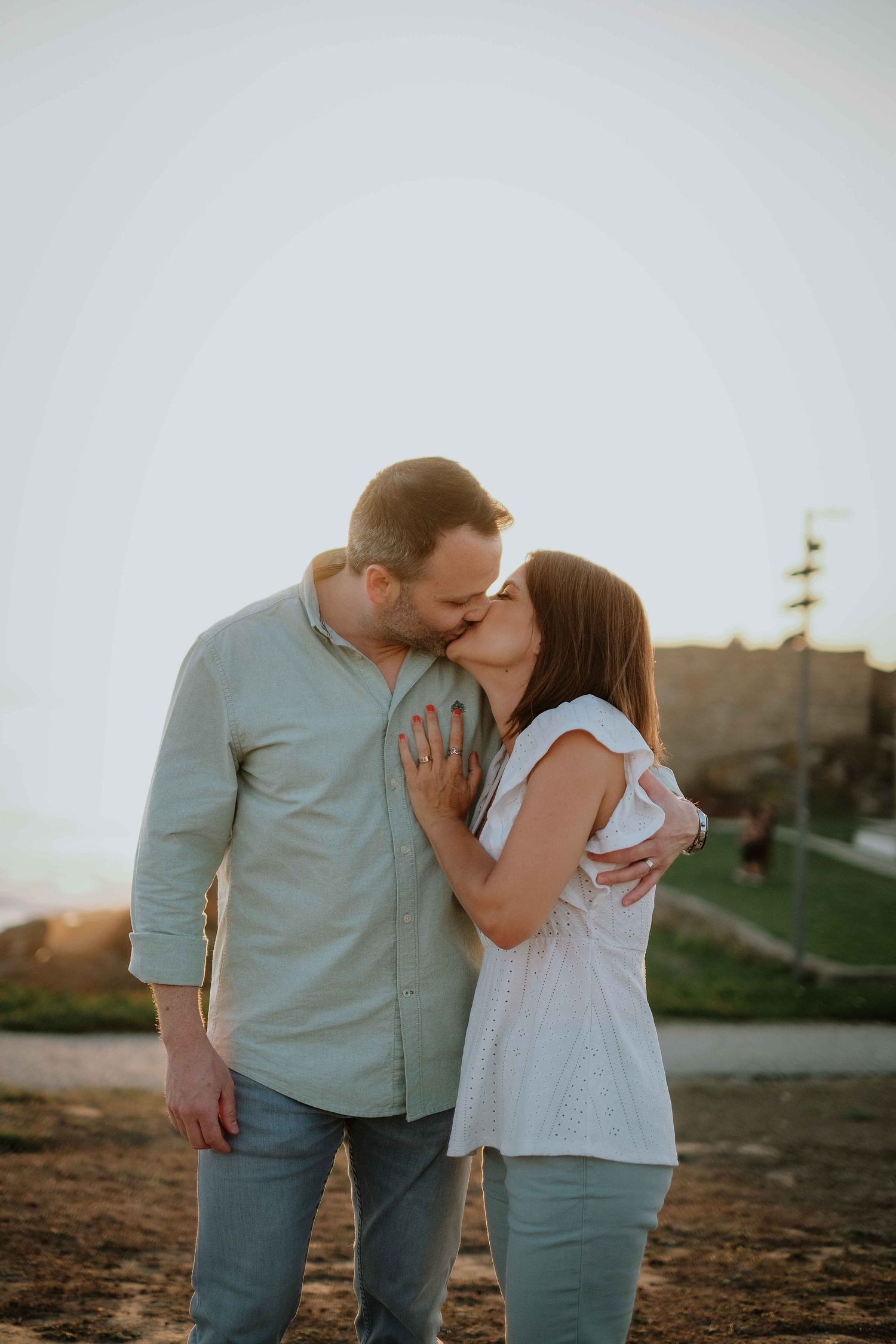 Couple sharing an intimate moment at sunset near coastal scenery.