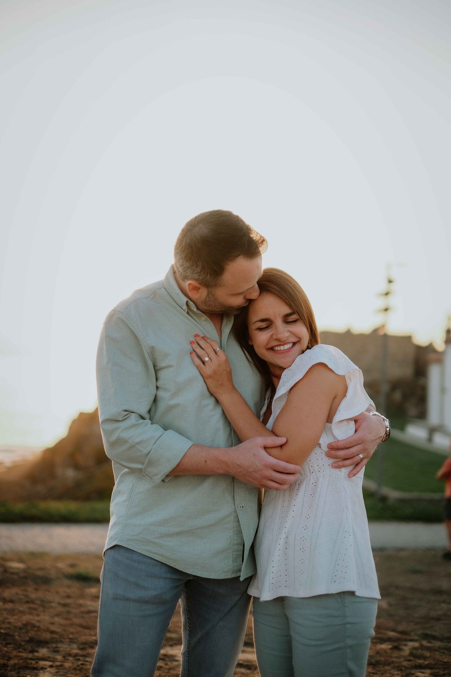 A couple embraces lovingly during a sunset photoshoot on a beach.