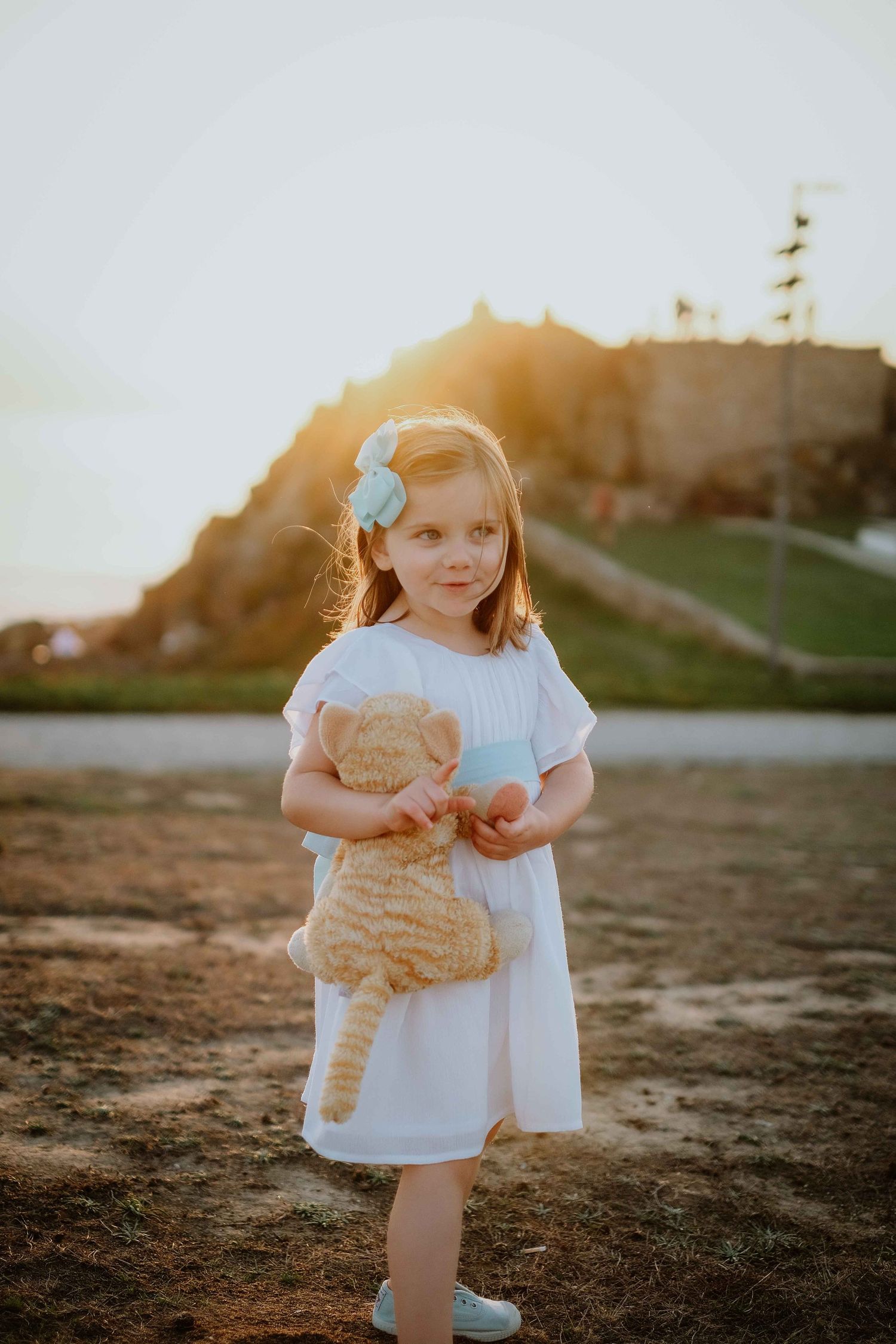 Child plays and poses in white dress during outdoor sunset photography session.