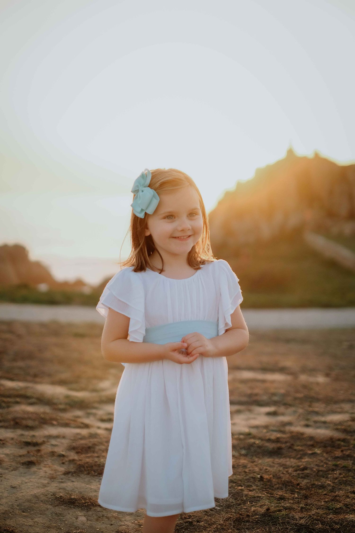 Young girl in white dress smiles during sunset photoshoot.