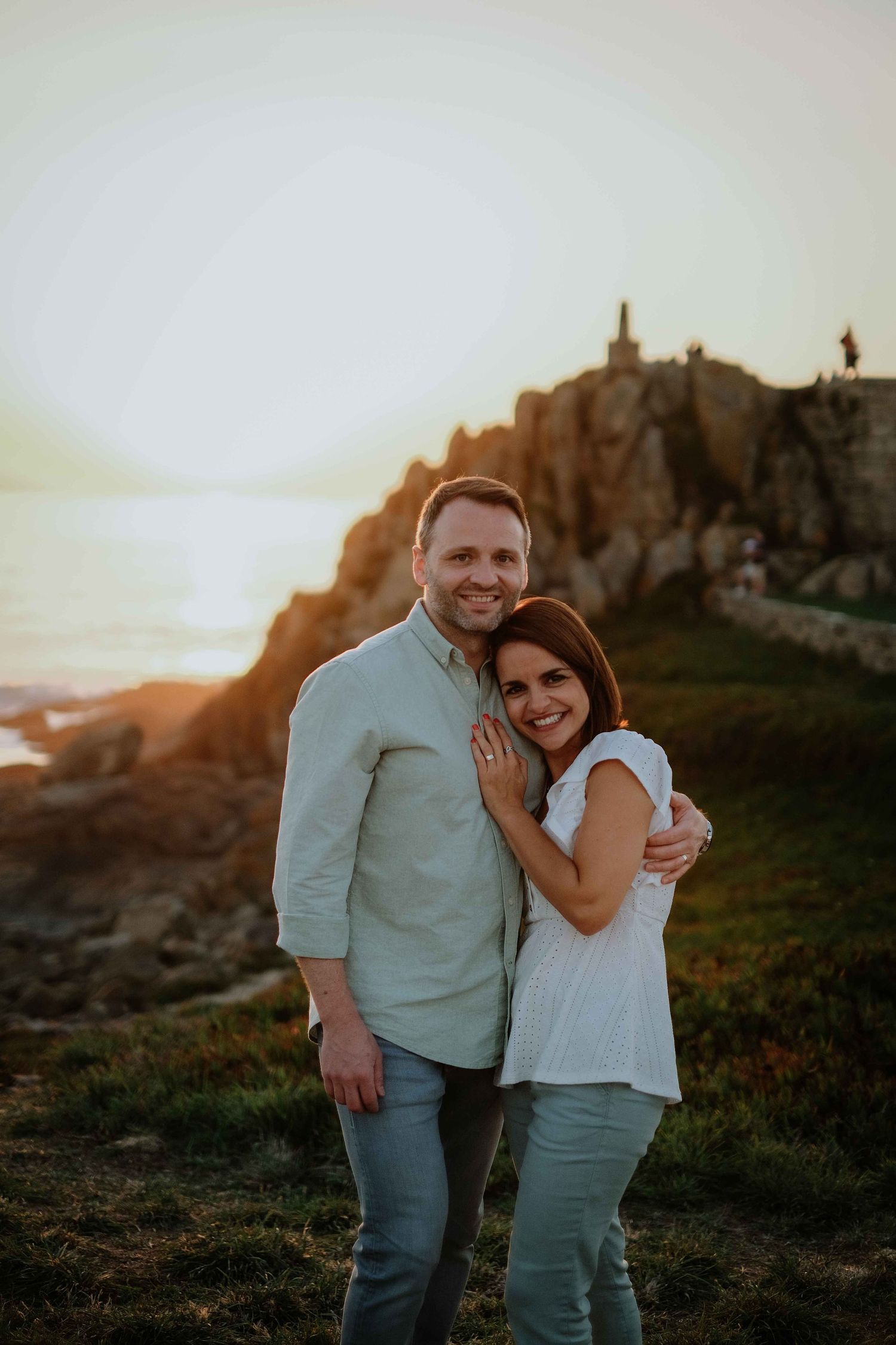 Couple shares intimate moment during sunset photoshoot on coastal hillside.