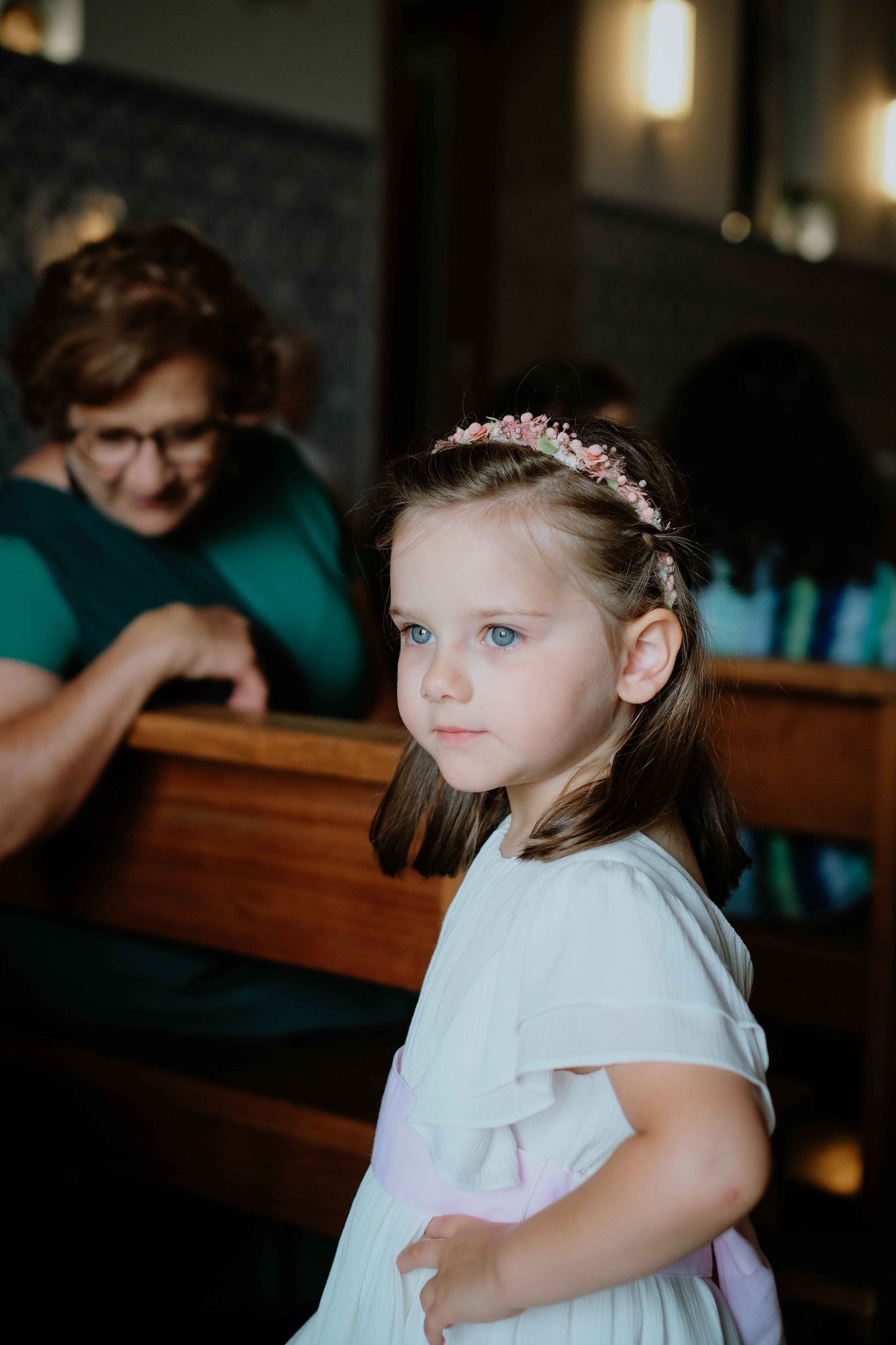 Child in formal white dress stands in church pew during ceremony.