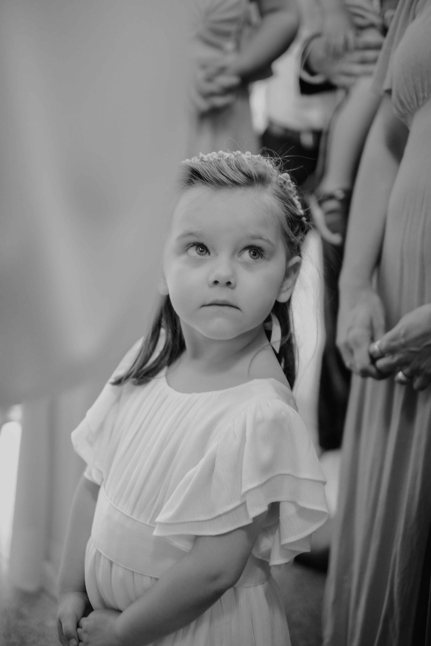 Child in white ruffled dress stands in formal setting during event.