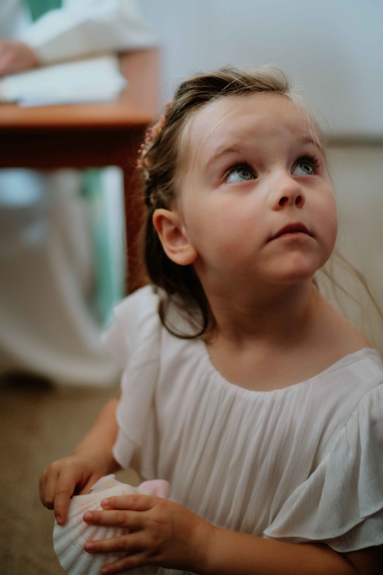 Young child in white dress looking upward with an innocent expression.