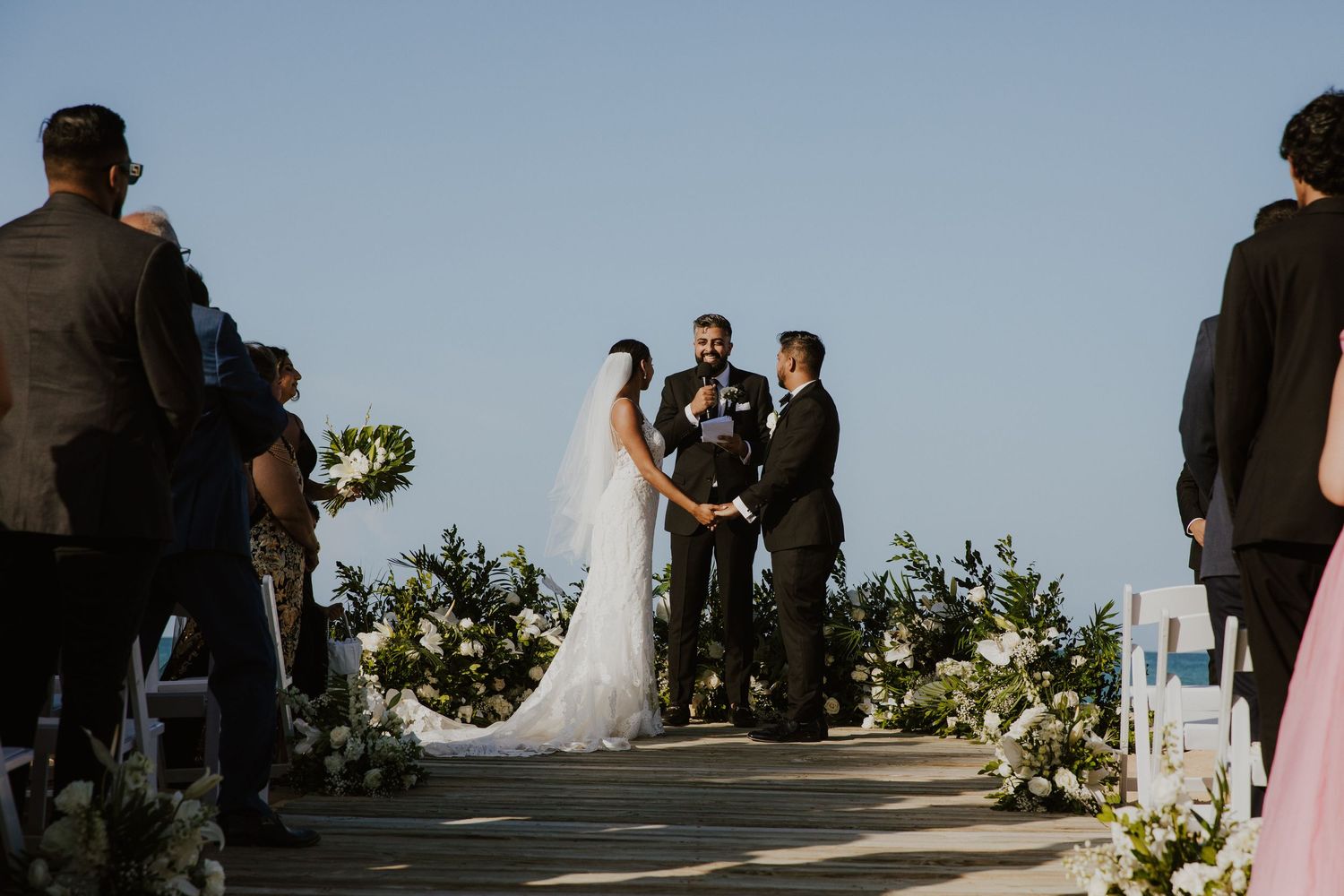 Outdoor beach wedding ceremony with guests seated and ocean view in background.