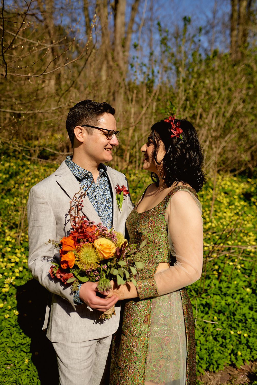 A couple exchanges loving glances while holding a bright fall bouquet in a sunlit garden.