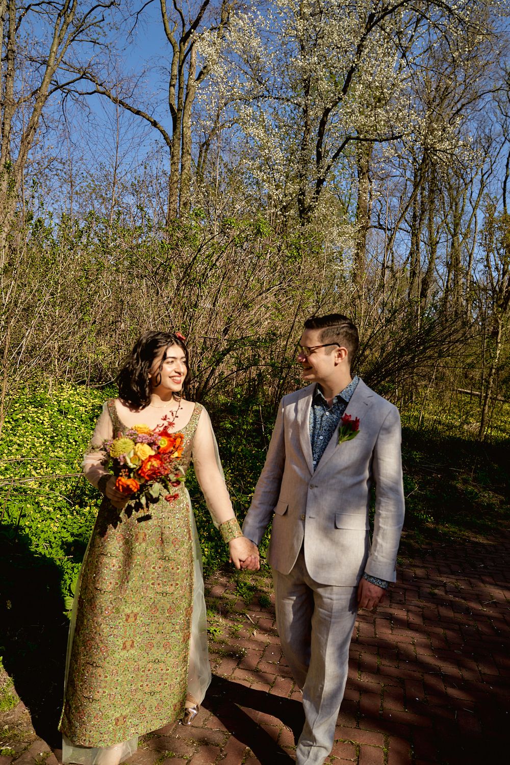 A couple walks hand in hand on a brick path through a spring garden.