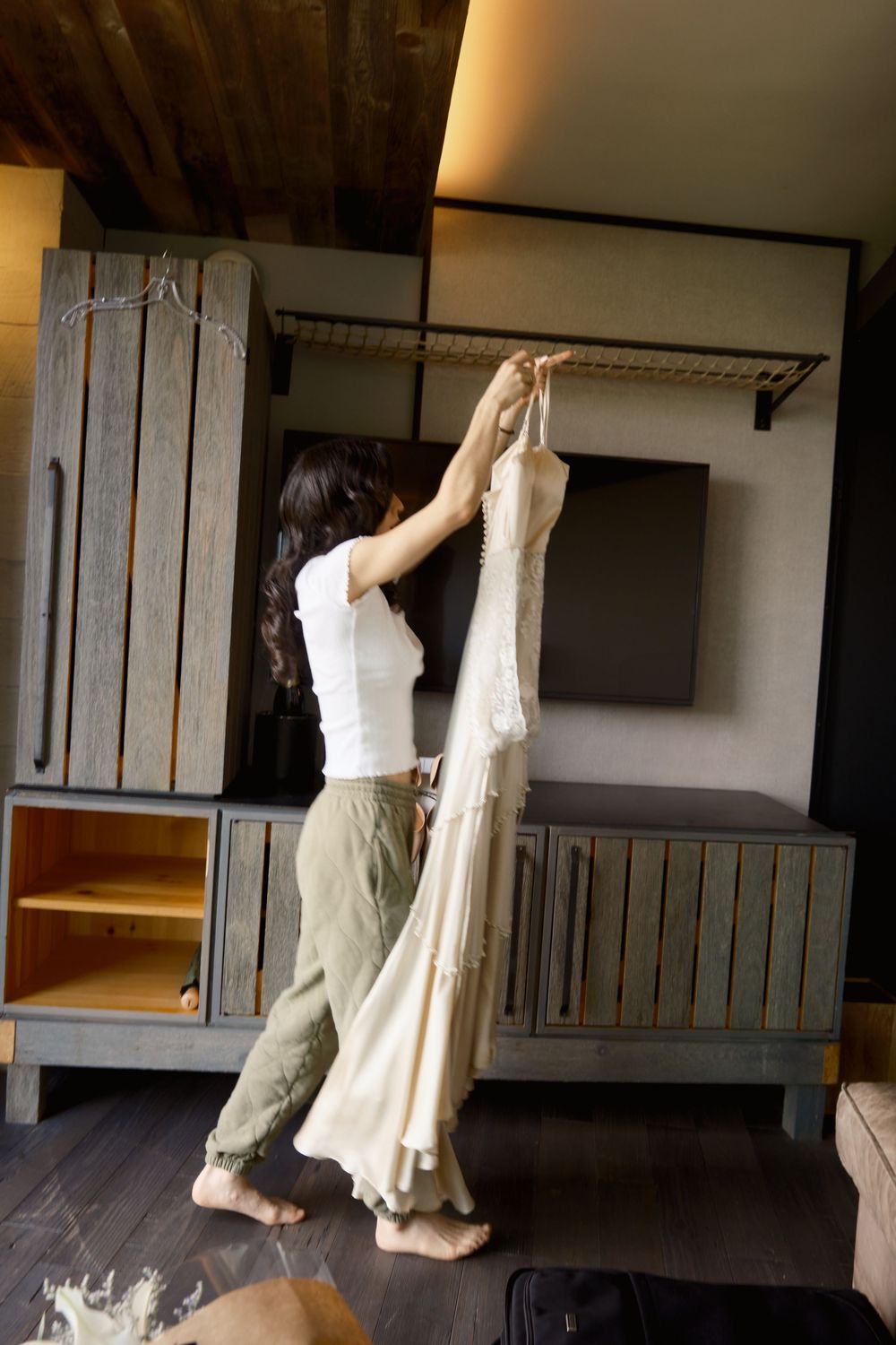 Someone in casual attire reaching up to adjust a white wedding dress hanging on display.
