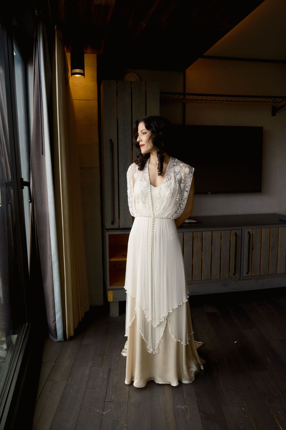 A flowing vintage-style wedding dress captured in natural window light against dark wood paneling at Mayson May