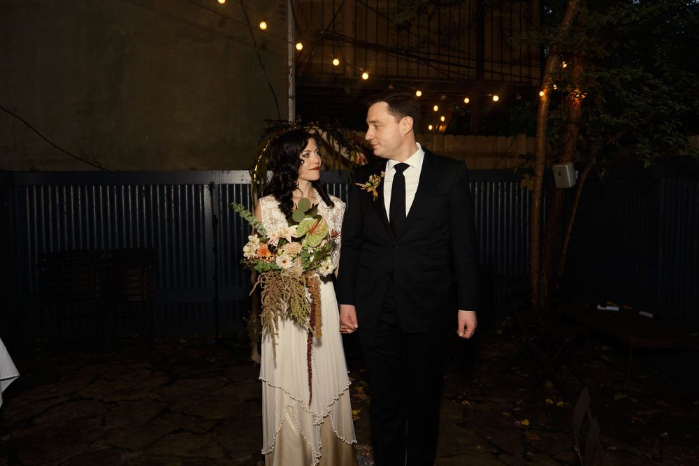 A couple in wedding attire shares an intimate moment under string lights in a garden setting at dusk at Mayson May