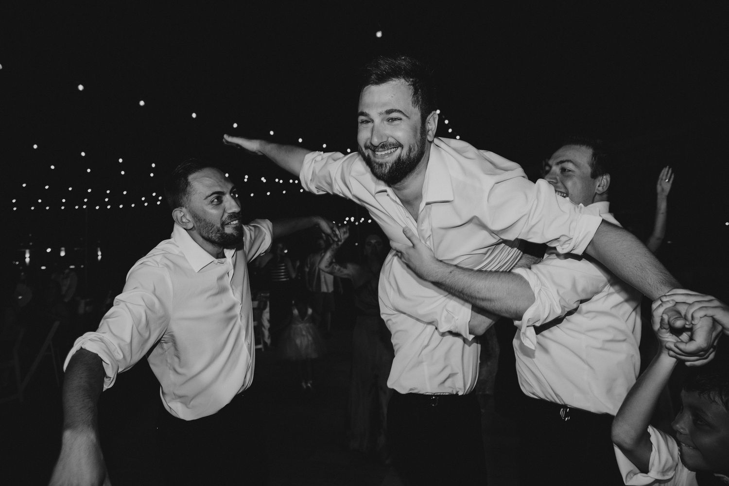 Wedding guests having fun dancing and celebrating at a nighttime reception with string lights overhead.