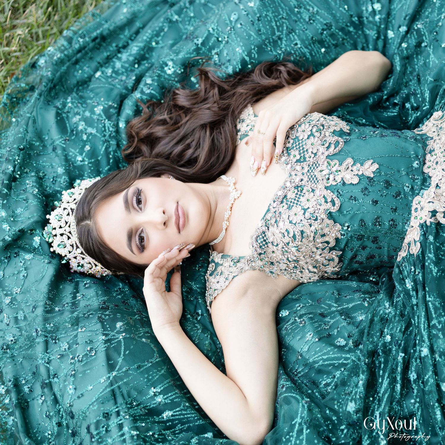 Someone wearing a white floral dress lies gracefully on emerald green velvet fabric creating a romantic portrait composition.