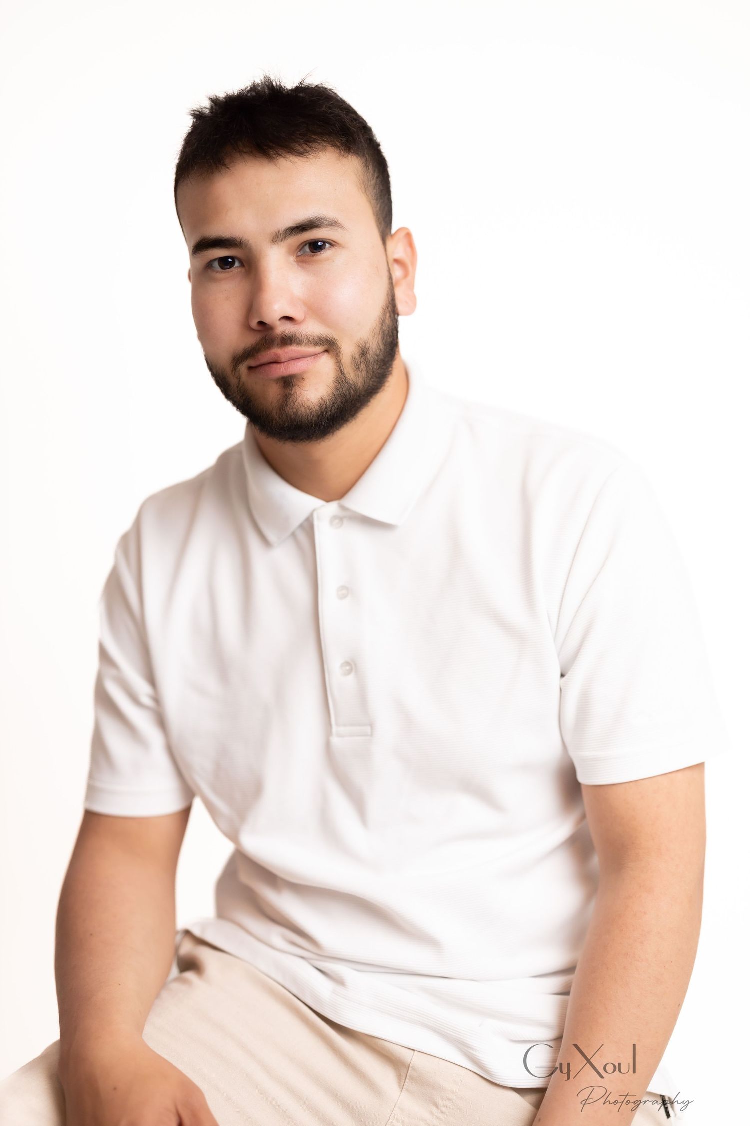 Person wearing a white polo shirt sits in a casual pose against a plain white background.