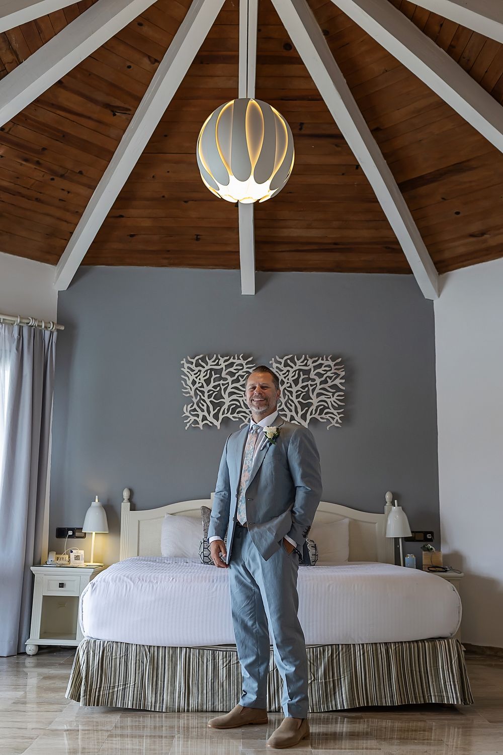 Modern bedroom interior features vaulted wood ceiling with white beams and spherical pendant light above striped bedding.